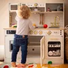 A young child is playing with a wooden toy kitchen. Produktbild-Vorschau