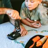 A man and a child are looking at a multi-tool being used on a toy car. Produktbild-Vorschau