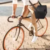 A person riding a bicycle on a brick-paved street, carrying a black cooler bag over their shoulder. Produktbild-Vorschau