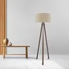 A floor lamp with a tripod base and a fabric shade stands next to a wooden bench with two decorative vases on it. Anteprima dell’immagine prodotto
