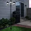 A black metal LED solar candelabra with three lights stands on a lawn in front of a house with a sliding glass door and a grill. Produktbild-Vorschau