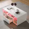 A modern white coffee table with integrated RGB LED lighting, placed on a patterned rug in a living room setting. Náhľad obrázku produktu