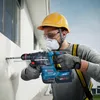 A construction worker is drilling a hole in a white wall with a power drill. Produktbild-Vorschau