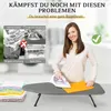 A woman is ironing on a small ironing board, with a stack of folded clothes next to it. The background shows a laundry room setting. Produktbild-Vorschau