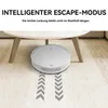 A white robot vacuum cleaner is shown on a carpeted floor, moving under a white coffee table. Gray chevron arrows indicate its path. Produktbild-Vorschau