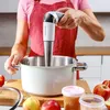 A person is using an immersion blender in a pot on a wooden cutting board, with apples and jars of food nearby. Náhled obrázku produktu