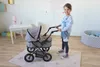 A young girl is playing with a doll stroller in a room. Produktbild-Vorschau