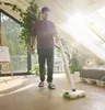 A man is cleaning a wooden floor with a cordless floor cleaner in a bright room with large windows and plants. Anteprima dell’immagine prodotto