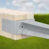 A close-up shot of a metal post anchor attached to a wooden post, set against a blurred background of sky and grass. Produktbild-Vorschau