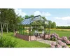 A greenhouse with a table and chairs inside, set in a garden with flowers and trees. Náhled obrázku produktu