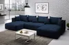 A navy blue sectional sofa is shown in a modern living room setting with large windows and a brick wall. Náhľad obrázku produktu