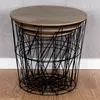 A set of three nesting tables with wooden tops and black wire basket bases, placed on a wooden floor against a textured gray wall. Produktbild-Vorschau