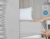 A hand is shown stretching a light gray fitted sheet over a mattress, with a pillow in the background. Produktbild-Vorschau
