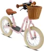 A pink balance bike with a brown seat and handlebars, and a wicker basket on the front. Produktbild-Vorschau
