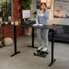 A woman is using a standing desk with a stepper, talking on the phone. Produktbild-Vorschau