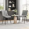 Two gray upholstered chairs flank a small round table with a vase of greenery and a cup of coffee, set in a room with a bookshelf and window. Produktbild-Vorschau