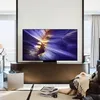 A modern living room with a large TV displaying a colorful abstract image, a leather armchair with a blanket, and a small metallic side table. Produktbild-Vorschau