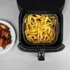 An overhead view of an open air fryer with a silicone liner filled with french fries. To the left, a white plate holds several chicken wings. Náhľad obrázku produktu