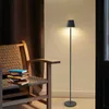 A floor lamp is placed next to a chair with books on it, in a room with brown curtains. Produktbild-Vorschau