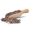 A wooden scoop filled with cocoa nibs, with some spilled onto a white surface. Náhled obrázku produktu