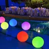 Fünf leuchtende LED-Poolleuchten in Pink, Gelb, Blau, Lila, Orange und Grün, die nachts in einem Schwimmbad schwimmen, mit einem Essbereich im Hintergrund Anteprima dell’immagine prodotto