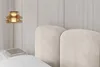 A close-up view of a bed with a beige upholstered headboard and a bedside table with a book and a pendant lamp. Produktbild-Vorschau