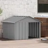 A grey dog house is shown outdoors on a wooden deck, with a brick wall and part of a wicker furniture set in the background. Náhľad obrázku produktu