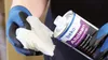 A person wearing blue and black gloves is holding a white cloth and a can of Beko Allclean surface cleaner. Produktbild-Vorschau