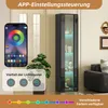A tall, narrow glass display cabinet with LED lighting, shown in a room setting with a plant and a sofa. A smartphone screen displaying lighting controls is also visible. Náhľad obrázku produktu