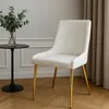 A cream-colored velvet chair with gold legs is shown in a room with a small black table and a vase of greenery. Náhľad obrázku produktu