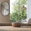 A modern living room with a large window overlooking trees, featuring a chair, coffee table, and a decorative mirror. Produktbild-Vorschau
