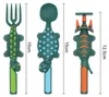 Three dinosaur-themed children's utensils (fork, spoon, and pusher) are displayed side-by-side against a white background. Measurement lines indicate their sizes. Produktbild-Vorschau