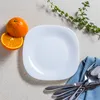 A white square plate with oranges and cutlery on a textured surface. Podgląd zdjęcia produktu
