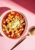 A bowl of lupini beans in a red sauce, topped with sour cream and green onions, with a golden spoon to the side. Produktbild-Vorschau