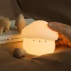 A hand is touching a mushroom-shaped night light that is lit up, with other wooden decorative items in the background. Podgląd zdjęcia produktu