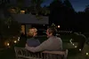 A couple sits on a bench in a garden at night, illuminated by outdoor lights. Produktbild-Vorschau