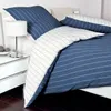 A neatly made bed with blue and white striped bedding and a white bedside table with a lamp. Produktbild-Vorschau