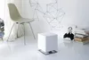 A modern, minimalist room with a white floor and wall, featuring a chair, a white cube-shaped object, and a stack of books. Produktbild-Vorschau