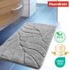 A grey bath mat with a leaf pattern is shown on a tiled floor next to a bathroom cabinet. Anteprima dell’immagine prodotto