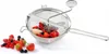 A stainless steel food mill filled with berries, with some berries scattered around it on a white background. Produktbild-Vorschau