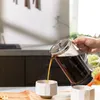 A person is pouring coffee from a French press into a mug in a kitchen setting. Produktbild-Vorschau