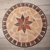 A top-down view of a round mosaic table with a star pattern in the center, set against a light wooden floor. Produktbild-Vorschau