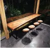 A long wooden table with four bar stools in front of a window overlooking lush greenery. Produktbild-Vorschau