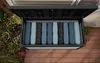An open storage box filled with cushions, placed on a wooden deck next to plants. Produktbild-Vorschau