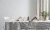 A table set with a white tablecloth, decorated with multiple candle holders and lit candles, with a chair in the foreground and curtains in the background. Podgląd zdjęcia produktu