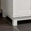 Close-up view of the white cabinet's base and legs on a dark tiled floor. Produktbild-Vorschau