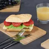 A sandwich and a glass of juice are placed on a wooden board, with grapes in the background. Produktbild-Vorschau