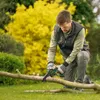 A man is using a small chainsaw to cut a branch in a garden. Podgląd zdjęcia produktu