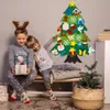 Two children in pajamas are sitting on a bench next to a DIY felt Christmas tree decorated with various ornaments. Produktbild-Vorschau