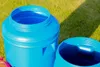 Two blue plastic barrels are shown outdoors on a grassy surface, with one barrel in the foreground and another to its right. Produktbild-Vorschau